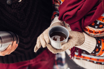 woman hands pours hot tea or coffee out of thermos on winter forest background. girl using a thermos in on a snowy day. metallic cup