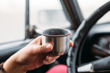 The driver in the car takes a thermos mug with a coffee bar so as not to fall asleep at the wheel. Man drinks coffee or tea in a car