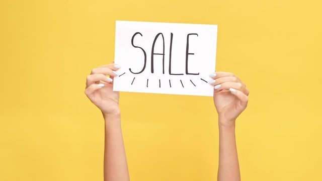 Woman hands holding nameplate SALE over yellow background
