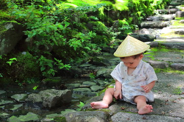 Little baby wearing a traditional yukata custom plays with forest leaves while sitting over the stone steps of Jojakko-ji temple`s main entrance stairs, Kyoto.