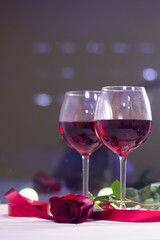 The concept of Love, Wedding, Proposal, Anniversary. A romantic evening with two glasses of red wine and a beautiful red velvet rose. Dark blurred background
