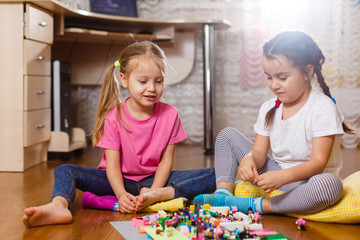 Fototapeta premium Two cute little children are playing with blocks happy girls at home funny lovely sisters