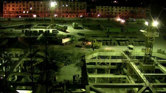 Construction of new shopping center by night. Foundation with parking level, crane, trucks and people working. In Shanghai construction sites are active day and night
