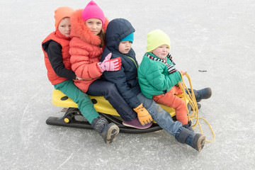 happy children in colorful clothes came with their parents to ride a sled. Emotional children enjoy a sunny afternoon and glide along the frozen lake's ice