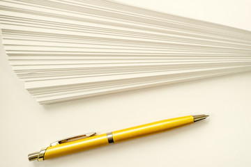 a stack of sheets of white paper and ball point gold pen