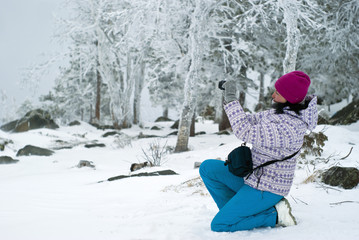 Fototapeta na wymiar woman photographer standing on one knee, shooting something on the background of a snowy winter forest in the mountains..