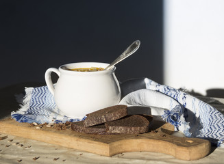 on table a blue napkin with ornament pattern and soup tureen with yellow soup in the sun bread wooden board seeds