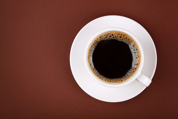 Full cup of black coffee in white cup on brown