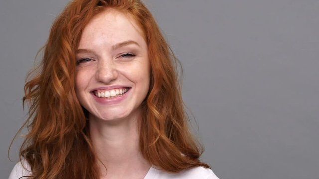 Close up view of cheerful mystery ginger woman in t-shirt showing her tongue and looking at the camera over gray background
