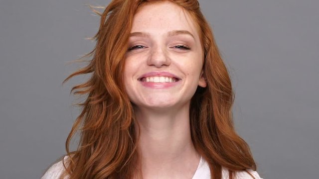 Close up view of smiling ginger woman in t-shirt looking at the camera over gray background