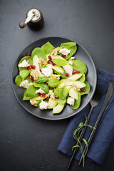Fresh useful vegetarian wholesome avocado, spinach, pomegranate seeds, walnut, saffron, pepper and ricotta salad on  black background. Selective focus. Top view. Copy space for text.