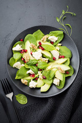Fresh useful vegetarian wholesome avocado, spinach, pomegranate seeds, walnut, saffron, pepper and ricotta salad on  black background. Selective focus. Top view. Copy space for text.