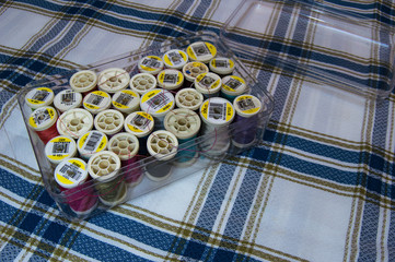 Plastic box filled with yarn spools of many colors on pretty checkered fabric.