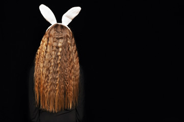 Young girl on a black background with ears of a hare on her head. Rear view