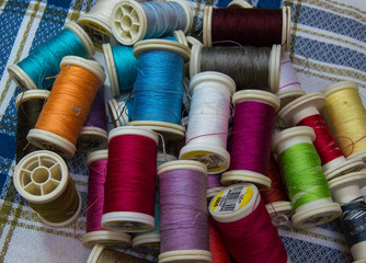 Mountain of colorful yarn spools of many colors on pretty checkered fabric. Tailoring material for sewing.