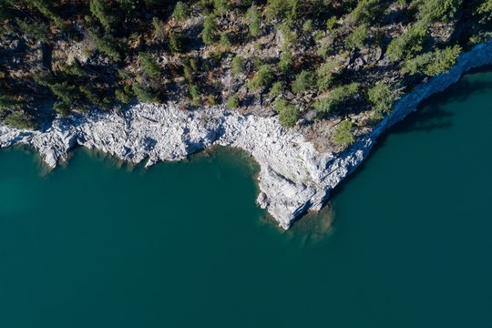 Fototapeta Rocky cliff and trees along the turquoise sea