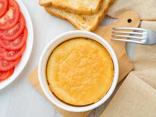 white round ramekin with oven-baked omelet of eggs and milk, with a crust, on white wooden table, top view.