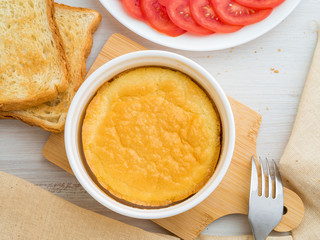 white round ramekin with oven-baked omelet of eggs and milk, with a crust, on white wooden table, top view.