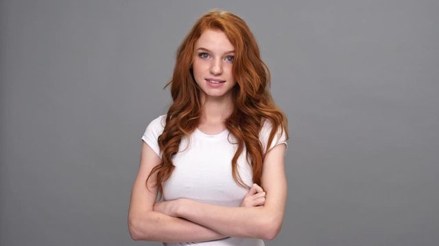Confused ginger woman in t-shirt with crossed arms saying oops over gray background