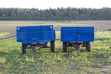 Two blue carts for tractors are in the garden in the village