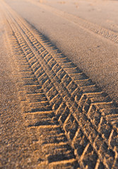 Tyre tracks going off in the distance on a golden sandy beach at sunset