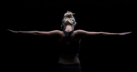Fototapeta na wymiar Beautiful fit and healthy blond woman in black top in dark with arms stretched from behind