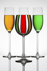 Wineglasses on a shiny surface with different colour fluids that distort reflection