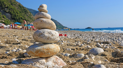 Fototapeta na wymiar Stones balance on beach, people sunbathe, swim and enjoy on sea vacation