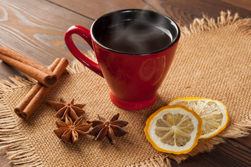 Red cup on burlap with coffee, spices and dried lemon on a wooden table