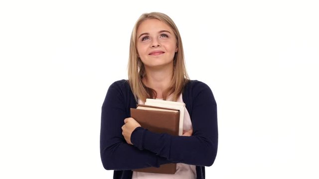 Pleased pensive blonde woman in cardigan holding books and looking up over white background
