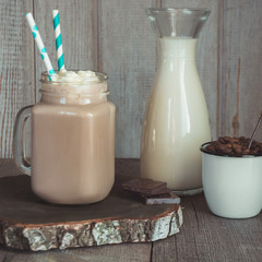 Chocolate coffee milkshake with whipped cream served in glass mason jar on gray wooden background. Sweet drink. Square image.