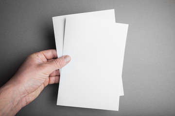 Hand holding white blank paper A5 sheet mockup. Leaflet document surface design.