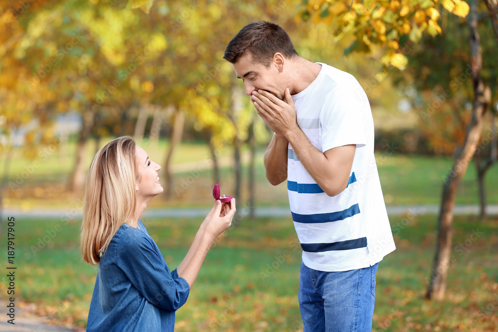 Wall mural young woman with engagement ring making proposal of marriage to her boyfriend in park