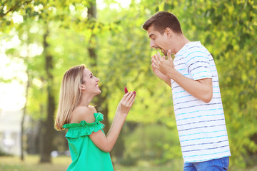 Fototapeta premium Young woman with engagement ring making proposal of marriage to her boyfriend in park