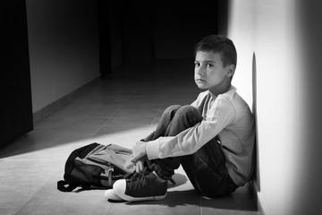 Upset little boy sitting in hallway, black and white effect