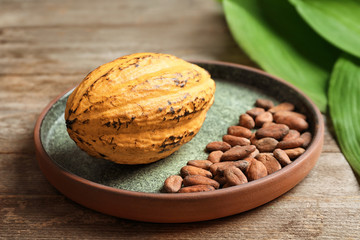 Plate with cocoa pod and beans on table, closeup