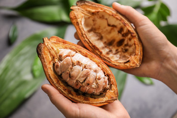 Woman holding cut cocoa pod on blurred background, closeup