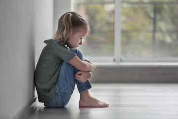 Sad little girl sitting on floor indoors