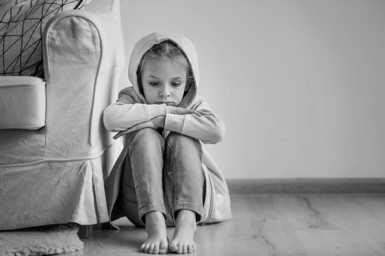 Sad little girl sitting on floor indoors, black and white effect