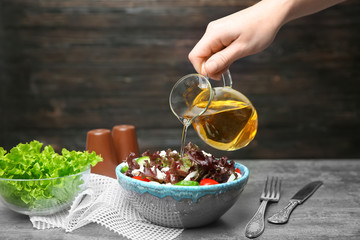 Woman adding tasty apple vinegar to salad with vegetables on table