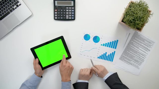 Businessmen analising diagrams in the office. A tablet with a green screen. View from the top of men's hands. Close-up shot.