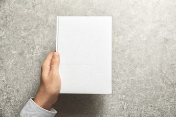 Man holding book with blank cover on grey background. Mock up for design