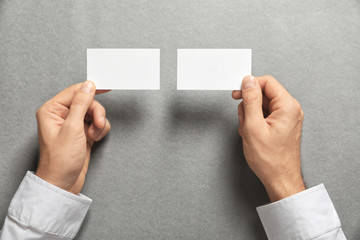 Man holding blank business cards on grey background. Mock up for design