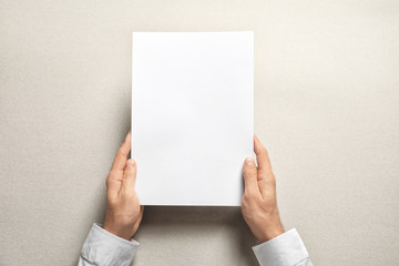 Man holding blank sheet of paper on light background. Mock up for design