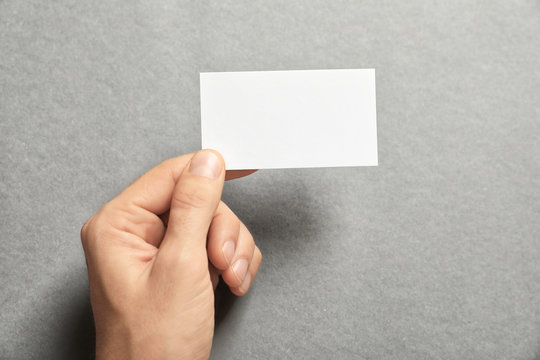 Man holding blank business card on grey background. Mock up for design