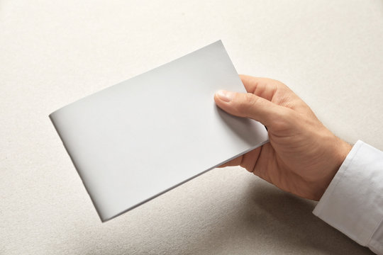 Man holding brochure with blank cover on light background. Mock up for design