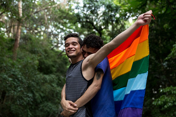 Gay Couple Embracing with Rainbow Flag in the Park