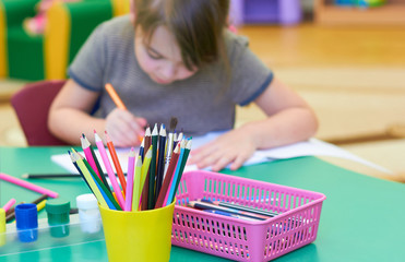 A cute little Caucasian girl draws at a table in a kindergarten.