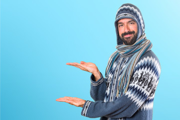 Man with winter clothes presenting something on colorful background