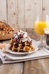 Sweet Belgian waffles for breakfast, decorated with white cream and chocolate sauce. A glass of coffee with black and orange juice, on a brown wooden background